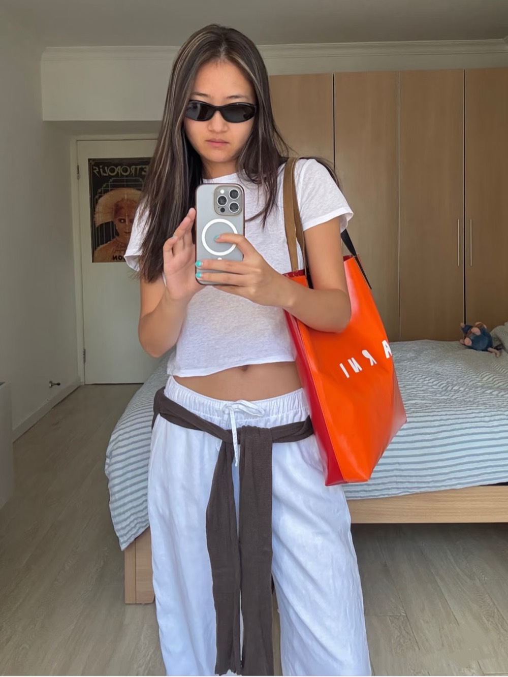 White tee with white linen trousers, a brown scarf tied at the waist and an orange patent tote